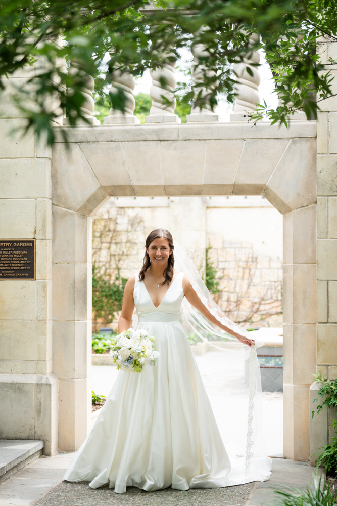 Hannah smiling in her gown with the Dallas Arboretum gardens behind her